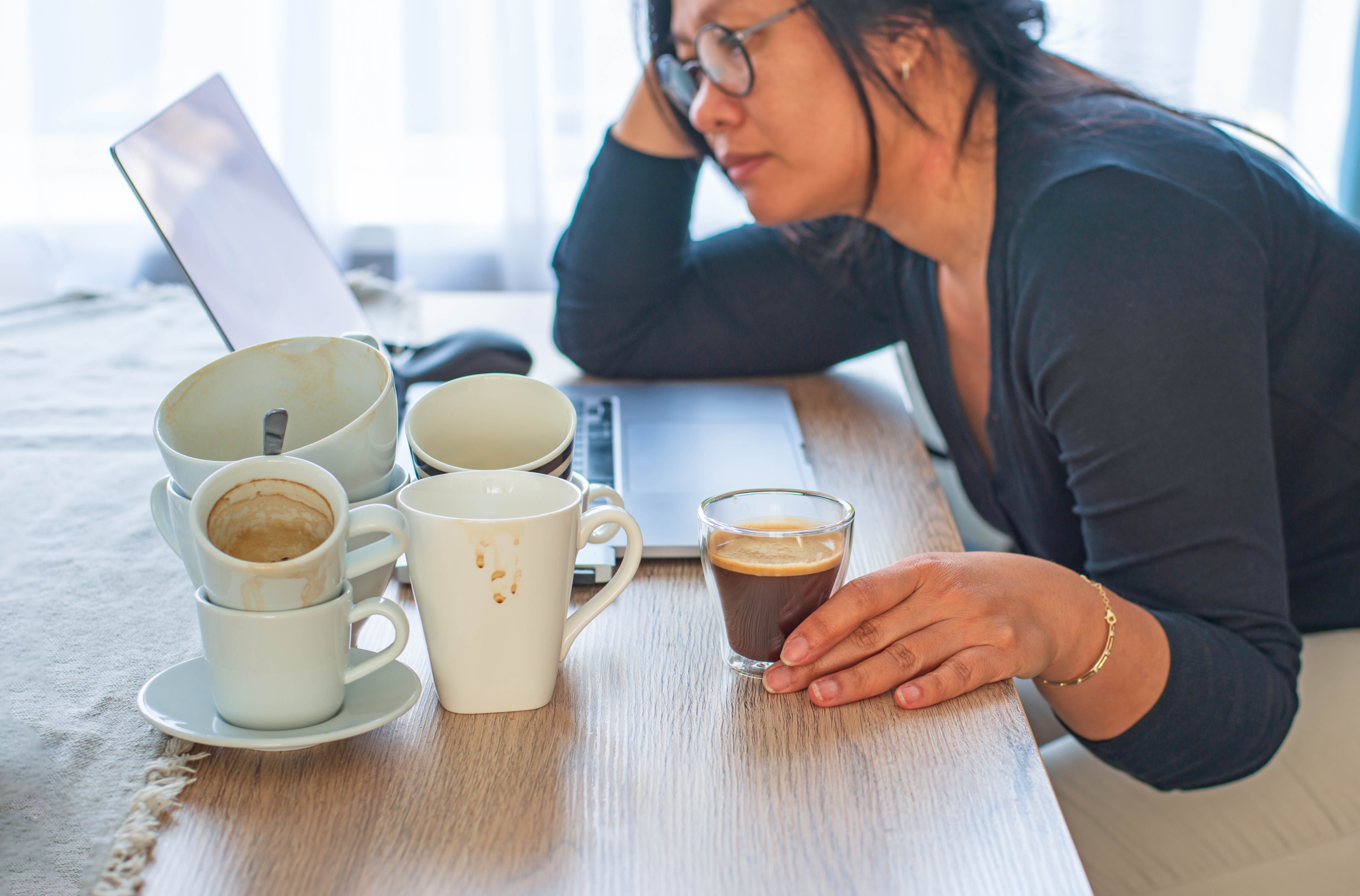 Woman at her laptop surrounded by empty coffee cups and an espresso Woman at her laptop surrounded by empty coffee cups and an espresso